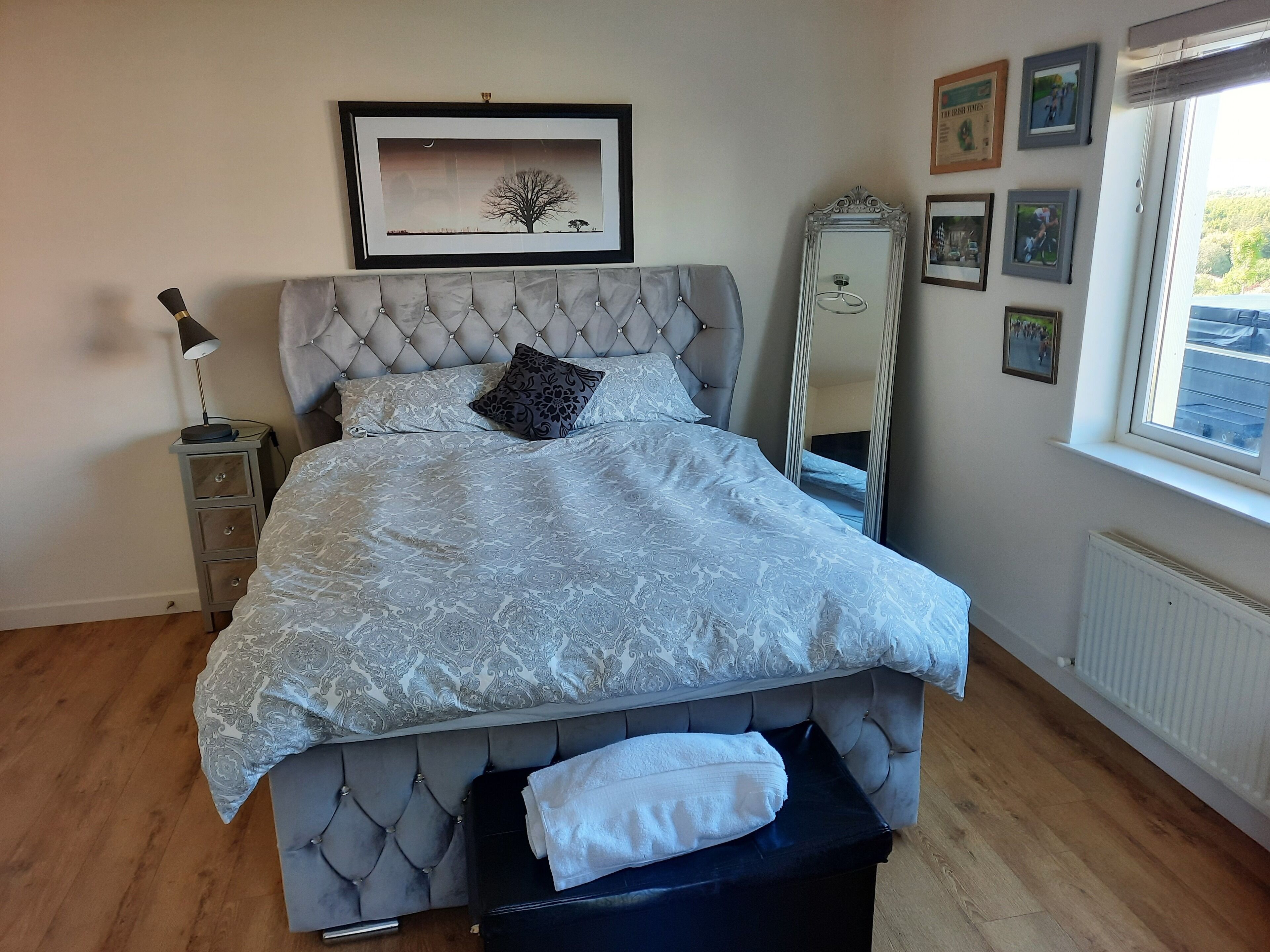 A neatly made bed with a patterned bedspread, a tufted headboard, and a bedside table with a lamp.
