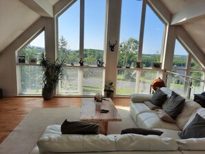 Ein geräumiger Raum mit großem Fenster, einem weißen Sofa, einem Holztisch und einem Blumentopf.