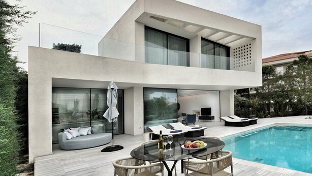 A modern two-story house with a swimming pool, outdoor seating, and a glass-enclosed patio.
