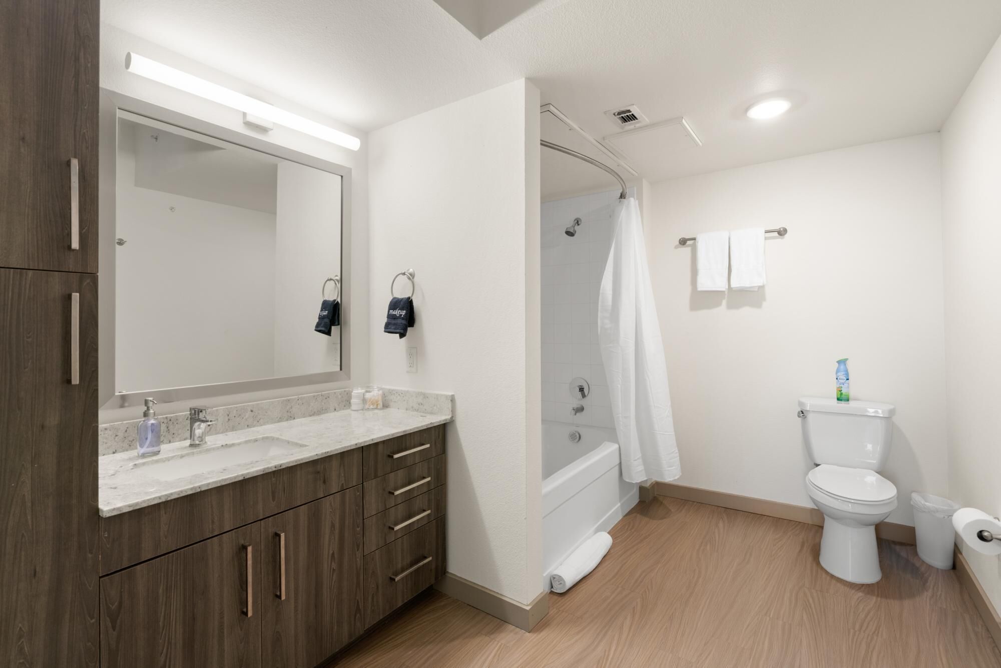 A modern bathroom with a wooden vanity, a large mirror, a shower, and a toilet.
