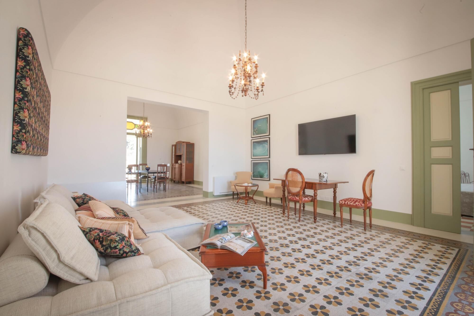 A spacious living room with a sofa, coffee table, and a dining area with chairs and a chandelier.