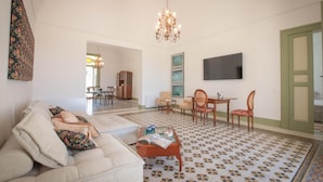 Ein geräumiges Wohnzimmer mit einer Couch, einem Couchtisch und einem Essbereich mit Stühlen und einer Kristallleuchtre.'