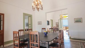 Ein Essbereich mit einer Chandelier, Holzstühlen, einem Tisch und Blick auf das Meer durch eine offene Tür.