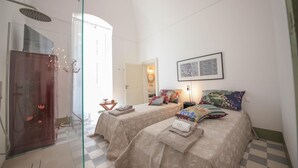 Ein Hotelzimmer mit zwei Betten, einer Duschkabine aus Glas, einem Schachbrettfußboden und einem gerahmten Kunstwerk an der Wand.