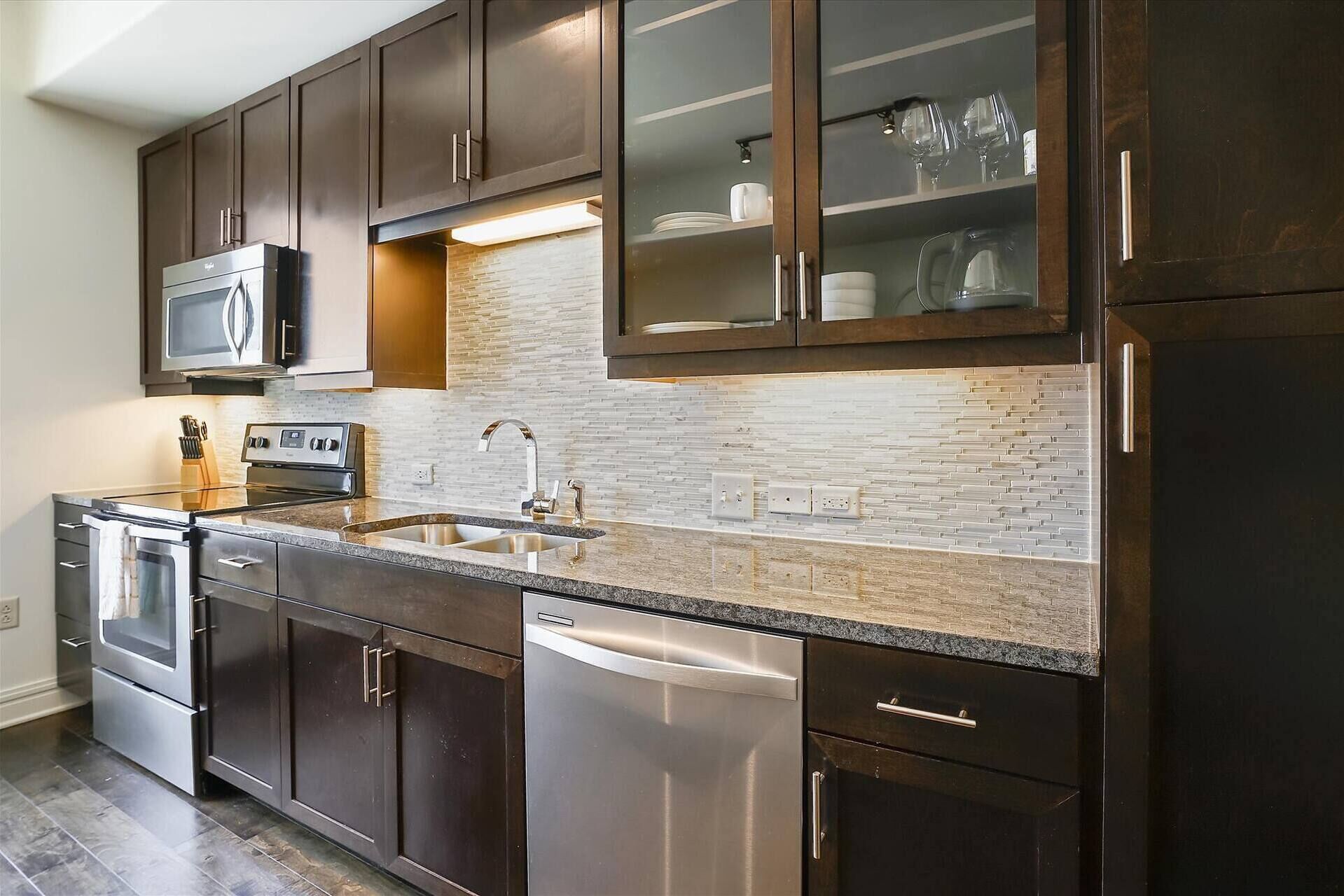 A modern kitchen with dark wooden cabinets, stainless steel appliances, and a tiled backsplash.