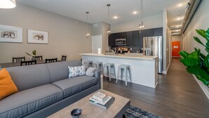 A modern living room with a grey sofa, a coffee table with books, and a kitchen area with a central island and bar stools. - Des Moines Alluring 2BD 2BA Downtown Apartment (Des Moines)