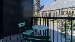 A balcony with a green bench and a small table, overlooking a historic building with a clock tower and a modern skyscraper in the background. - Des Moines Alluring 2BD 2BA Downtown Apartment (Des Moines)