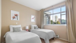 Een hotelkamer met twee bedden, beige wanden en een groot raam met uitzicht op gebouwen.