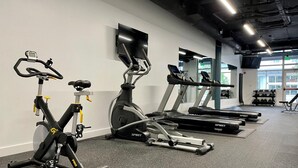 Ein Fitnessstudio mit Ergometer, Laufbändern und einem an der Wand montierten Fernseher.