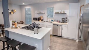 Une cuisine moderne avec des meubles blancs, un îlot central, des appareils électroménagers en acier inoxydable et un lave-vaisselle.