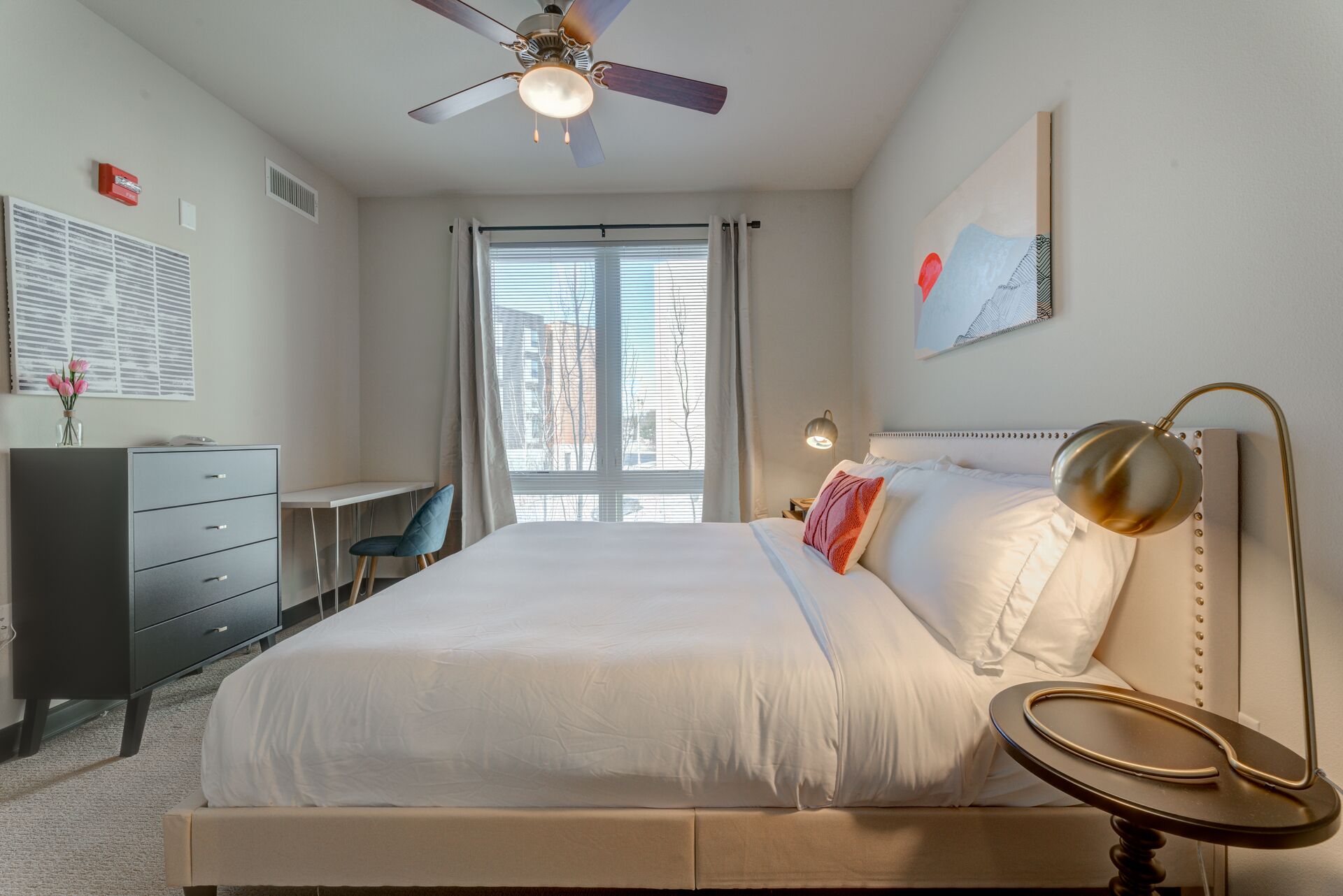 A hotel room with a bed, desk, chair, and a ceiling fan.