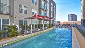 A swimming pool with lounge chairs and a covered seating area, surrounded by a multi-story building with balconies. - Dallas Beautiful 1BD 1BA Downtown Apartment (Dallas)