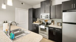 A modern kitchen with dark cabinets, stainless steel appliances, a granite countertop, and pendant lighting. - Dallas Beautiful 1BD 1BA Downtown Apartment (Dallas)