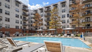 A rooftop pool area with lounge chairs and umbrellas, surrounded by multi-story buildings with balconies.