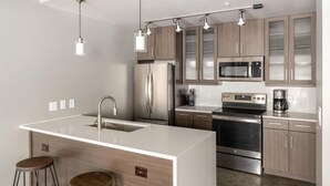 A modern kitchen with stainless steel appliances, wooden cabinets, and pendant lighting.