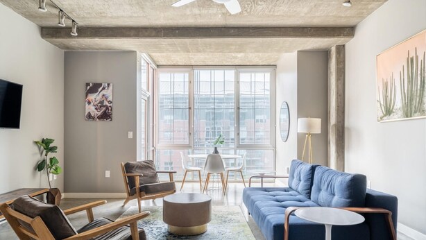 A modern living room with a blue sofa, wooden chairs, a round coffee table, and a dining area with a white table and chairs.