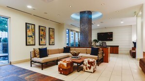 A spacious living area with a sectional sofa, two ottomans, a coffee table, and a fireplace. There are framed artworks on the wall and a flat-screen TV mounted above the fireplace. - Austin Awesome Studio Apartment (Austin)