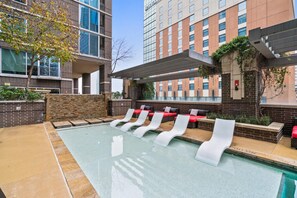 A modern outdoor pool area with lounge chairs and a stone wall. - Austin Awesome Studio Apartment (Austin)