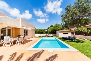 Une piscine entourée de chaises longues et d’une table, le tout bordé d’une pelouse bien entretenue et d’un bâtiment à la façade blanche.