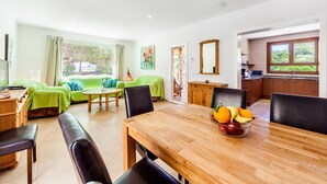 Ein modernes Wohnzimmer mit Esstisch, sofas in Grün, einer Küchenzeile und einem großen Fenster.