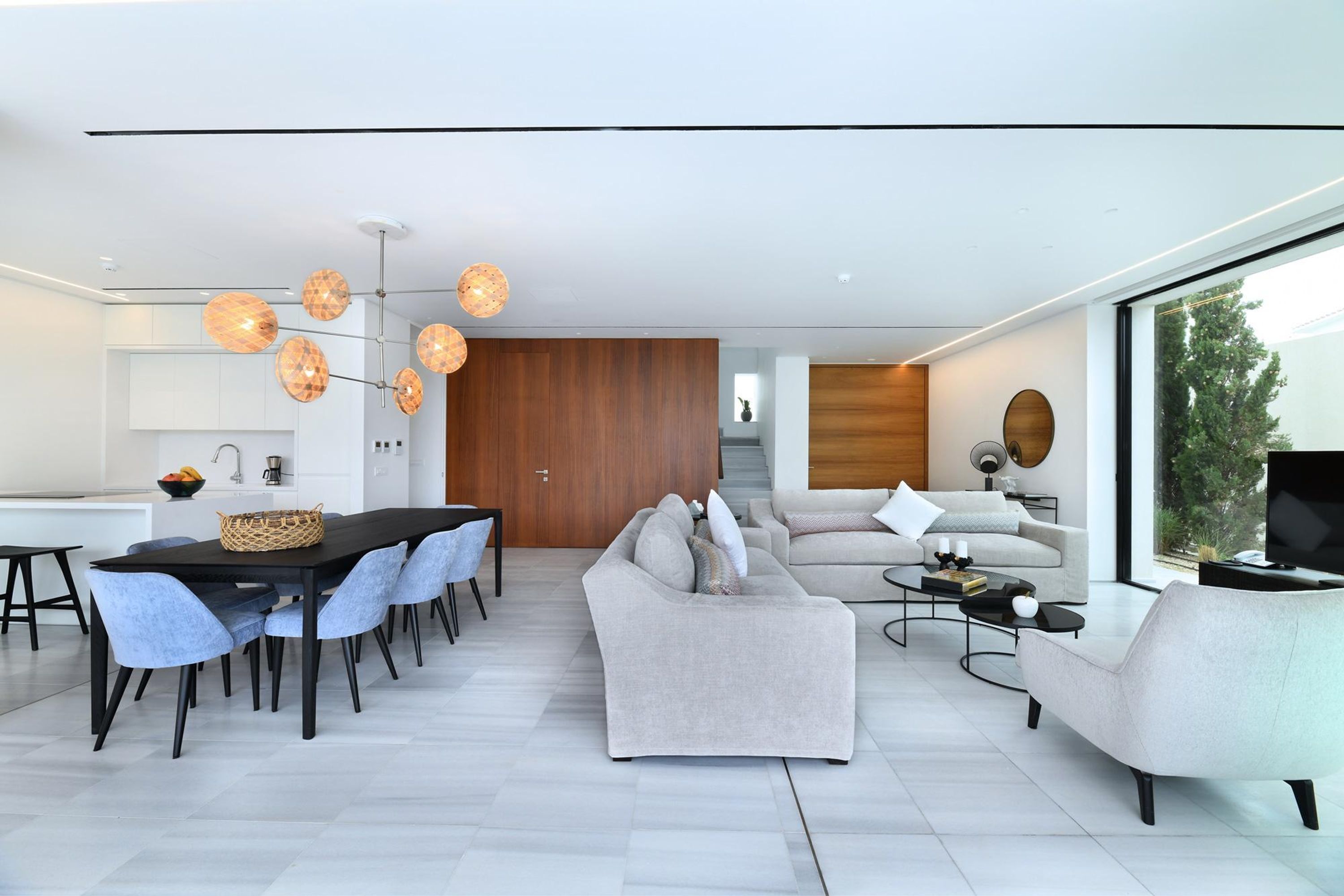 A modern living room with a dining area, featuring a large window, a sofa, a coffee table, and a TV.