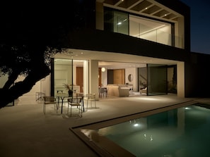 Une maison moderne à deux étages, dotée d’une piscine, de portes vitrées donnant sur un coin repas et d’un escalier apparent.