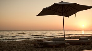 En strandscen med en solnedgång, två solstolar, ett parasoll och ett litet bord med en flätad korg.