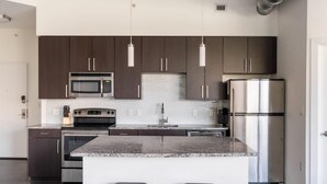 A modern kitchen with dark cabinets, stainless steel appliances, a granite countertop, and pendant lighting. - Alexandria Alluring 2BD 2BA Apartment (Alexandria)