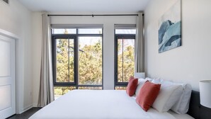 A bedroom with a large bed, two windows, a painting on the wall, and a bedside table. - Alexandria Alluring 2BD 2BA Apartment (Alexandria)
