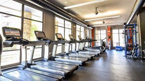 Une salle de sport dotée de plusieurs tapis de course alignés le long du mur, d’un espace dédié à la musculation et de grandes fenêtres laissant entrer la lumière naturelle.