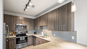 A modern kitchen with dark wood cabinets, stainless steel appliances, and a grey tiled backsplash.