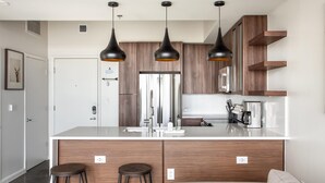 A modern kitchen with wooden cabinets, a stainless steel refrigerator, and black pendant lights.