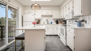 Une cuisine moderne avec des meubles blancs, un îlot central et une grande fenêtre donnant sur une terrasse.