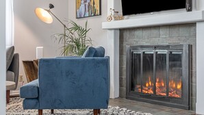 Un salon avec un canapé bleu, une cheminée, un téléviseur et un tableau accroché au mur.