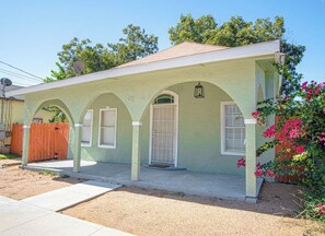 A single-story house with a porch, a front door, and a small garden with pink flowers. - 3 BR 1 BA Remodeled Home Near Downtown (San Antonio)