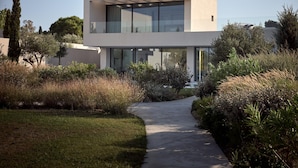 A modern two-story house with large glass windows and a concrete pathway leading to the entrance. - Butterflies Villas Spa-villa Plumeria (Zakynthos)