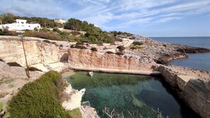 A coastal area with rocky cliffs, clear water, and a small boat anchored near the shore. - Casa Marieli - A 50 m dal Mare con Spazio Esterno (Gagliano del Capo)