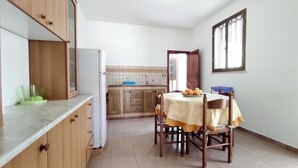 A compact kitchen with wooden cabinets, a white refrigerator, a tiled backsplash, and a dining table with chairs. - Casa Marieli - A 50 m dal Mare con Spazio Esterno (Gagliano del Capo)