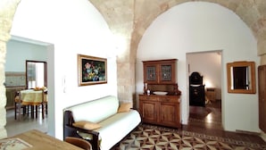 A living room with a sofa, a wooden cabinet, and a dining area with a table and chairs. - Casa Marieli - A 50 m dal Mare con Spazio Esterno (Gagliano del Capo)