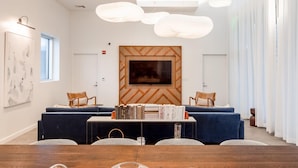 A modern conference room with a wooden accent wall, a large flat-screen TV, and a table with books and magazines. - Austin Awe-inspiring 1BD 1BA 2nd Street District Apartment (Austin)