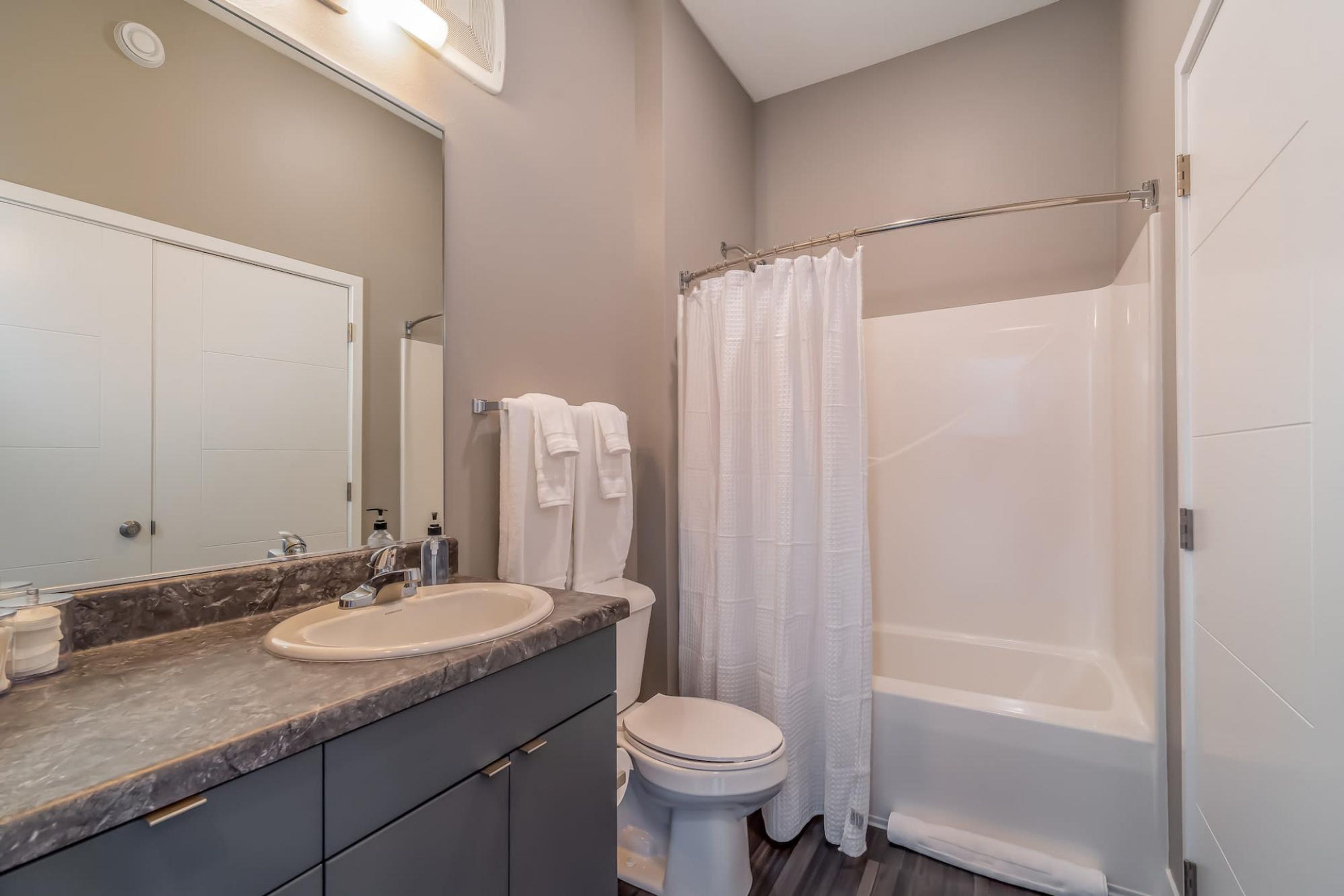 A modern bathroom with a marble countertop, a white sink, a toilet, and a walk-in shower with a curtain.