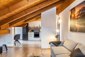 Une chambre aménagée sous les combles, avec un plafond en pente, un canapé, un bureau et, au fond, une cuisine.