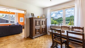 Una habitació amb un sofà, taula de dinar amb cadires, un armari i una finestra que dona a zona verda.
