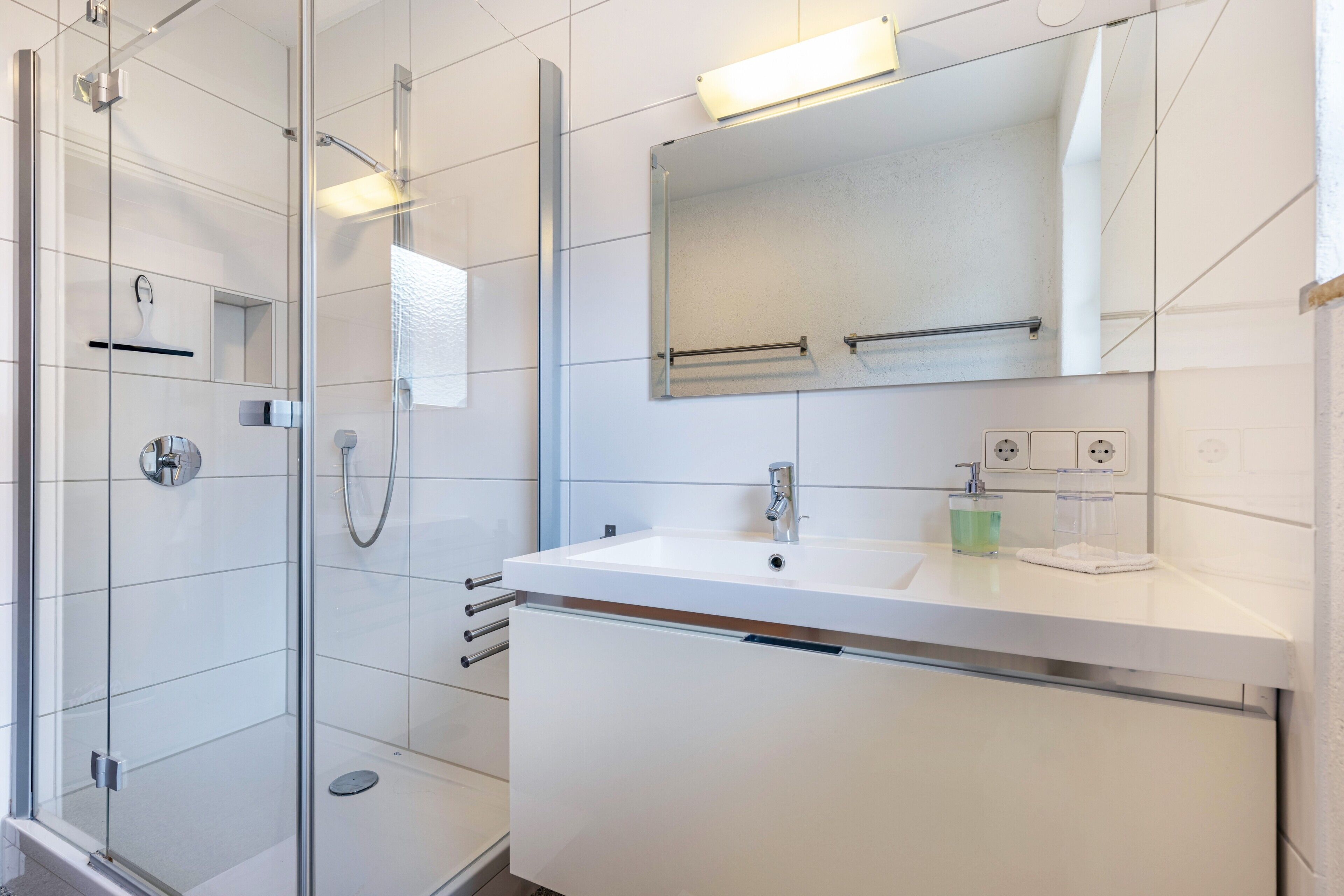 Un bagno moderno con box doccia in vetro, lavandino bianco e uno specchio grande.