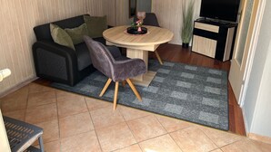 Ein kompakter Wohnbereich mit einer Couch, einem Esstisch, einem Fernseher und einer kleinen Küchenzeile.