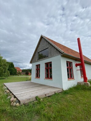 Ein eingeschossiges Haus mit einem geneigten Dach, einer Holzterrasse und einem roten Schornstein.