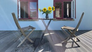 Eine Holzterrasse mit zwei Stühlen und einem Tisch mit einer Vase voller Sonnenblumen.