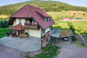 Une maison avec un toit en pente, une véranda et une voiture garée dans l’allée.