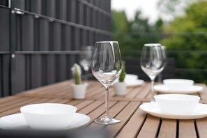 Een houten tafel met witte borden en transparant glaswerk, voor een donkere wand met beplanting op de achtergrond.