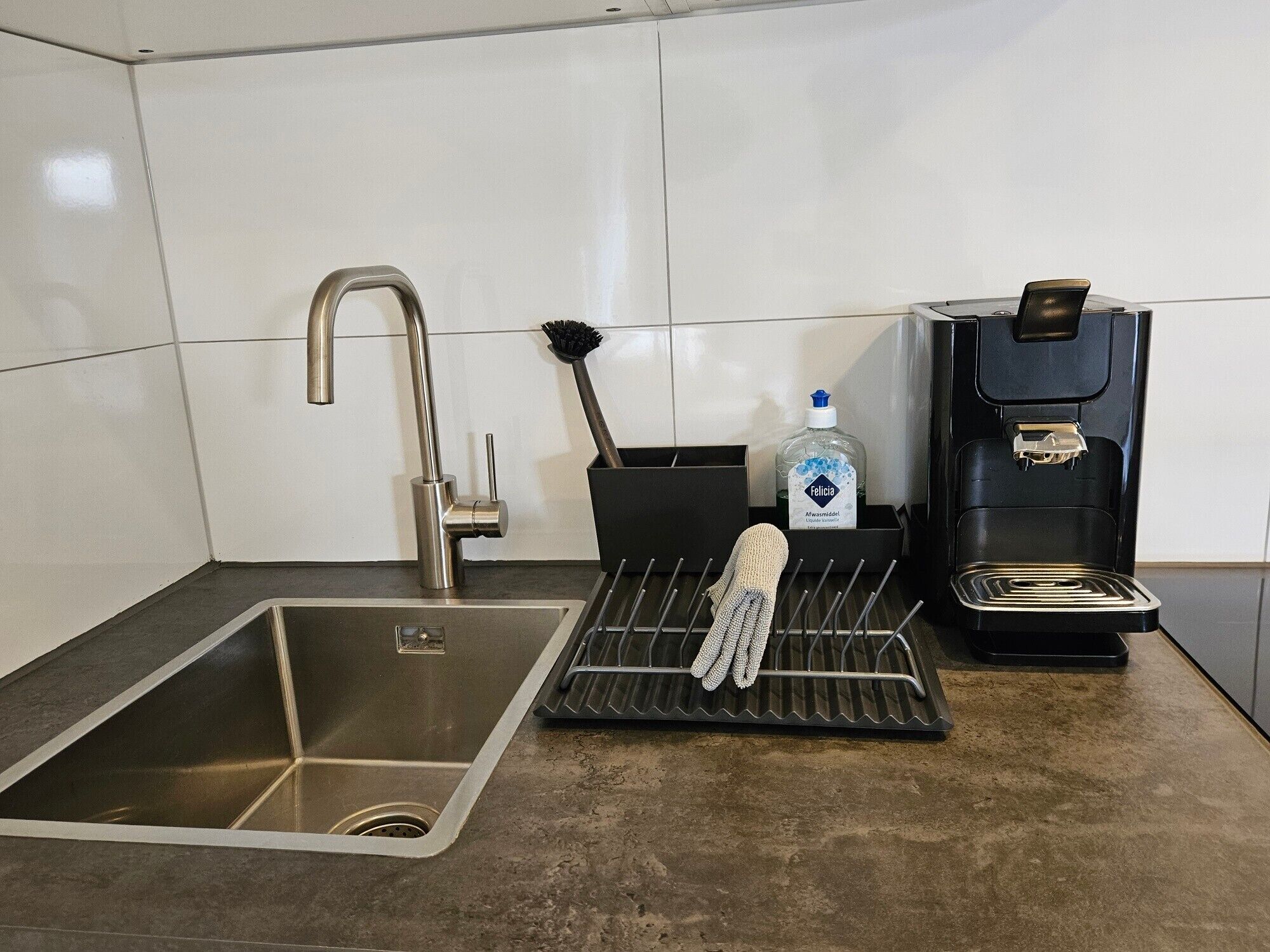 Una cucina moderna con lavello in acciaio inox, una macchina da caffè e uno scolapiatti.